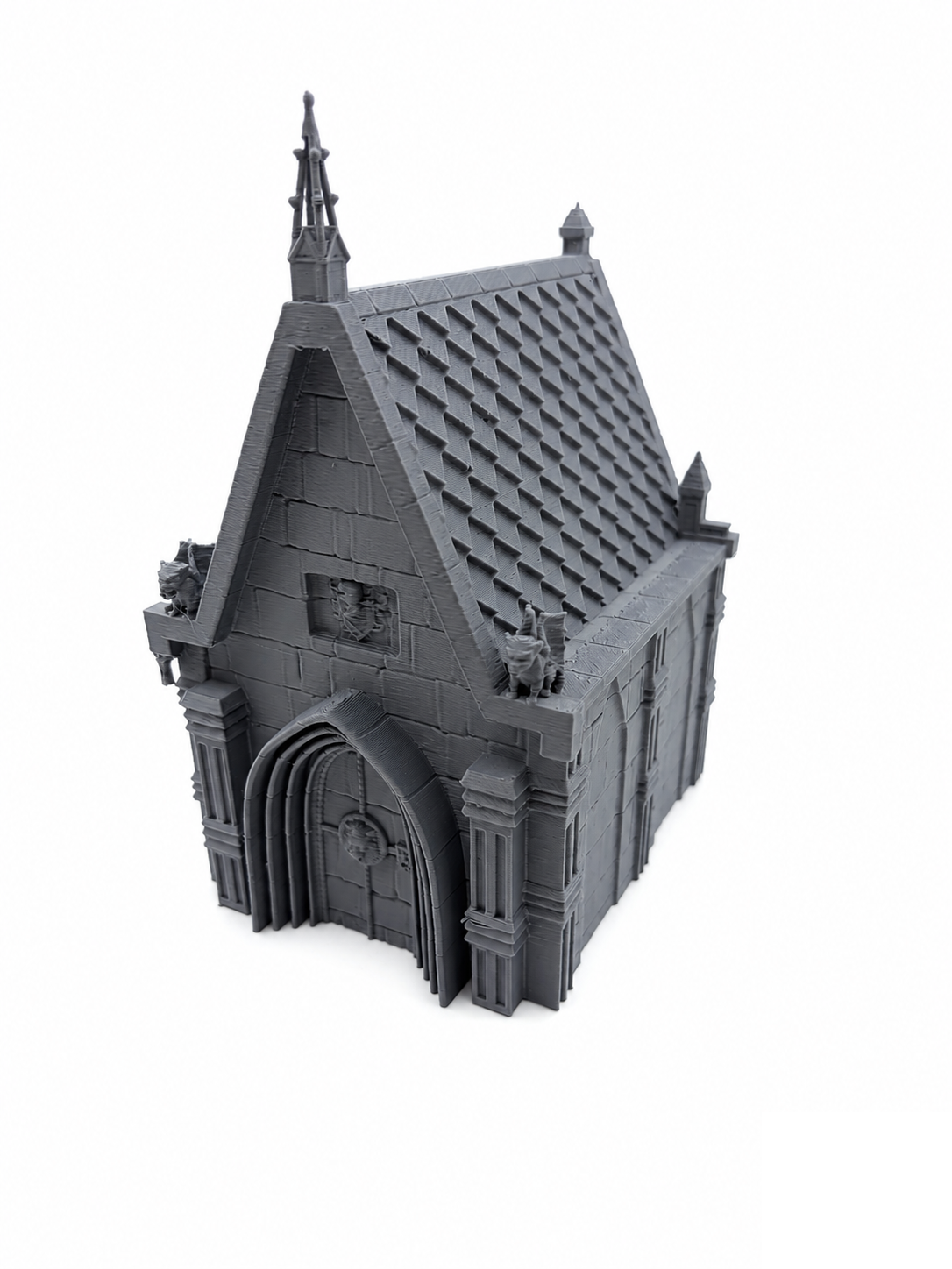 28mm gothic chapel terrain piece, 3D printed in grey PLA, with a steep shingled roof, spire finial, deep arched entrance and corner gargoyles